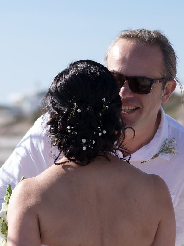 Bride with a low textured updo dotted with baby's breath, seen from behind on the beach