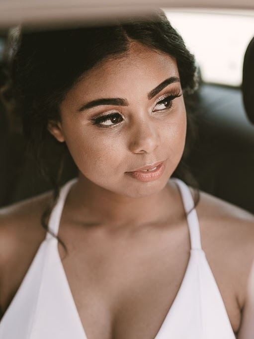 Bride gazing out of a car window with soft glowing makeup and defined brows